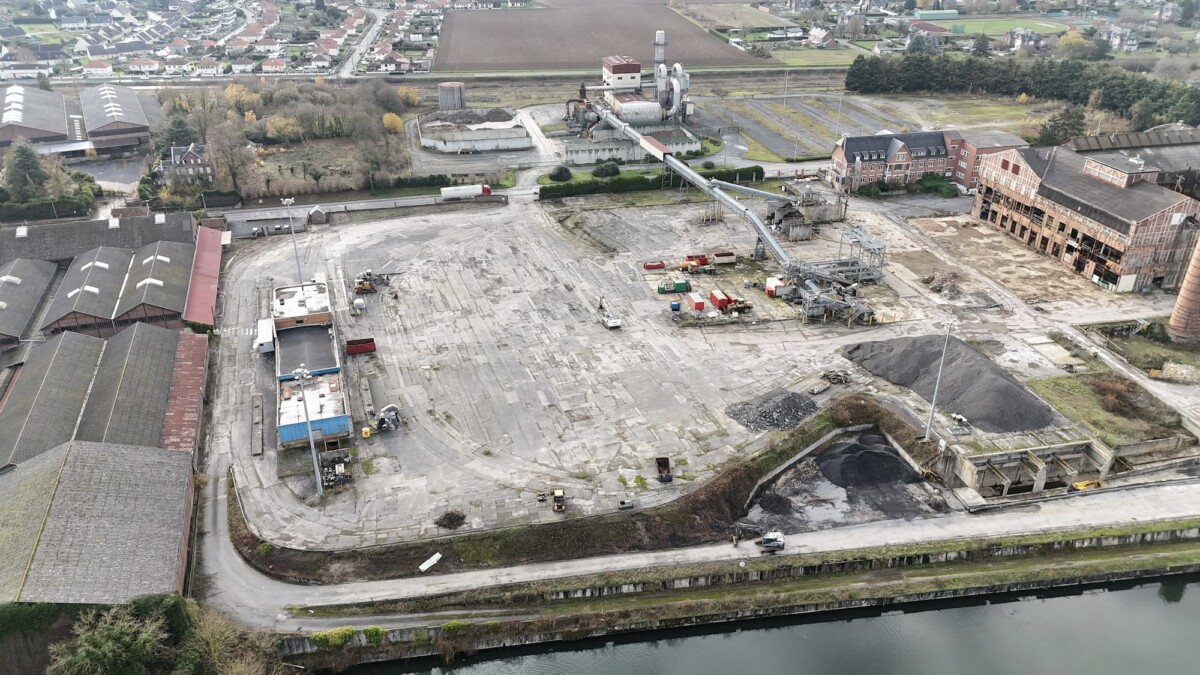 Plateforme Eppeville Excavatrice jaune déchargeant des déblais sur une péniche, avec des tas de gravats et des conteneurs en arrière-plan sur le chantier d'Eppeville.